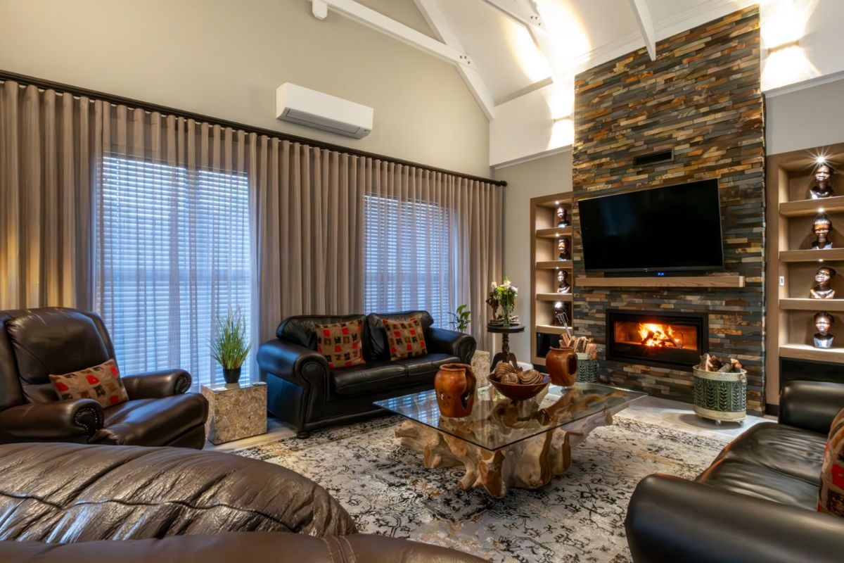 Spacious living room featuring a vaulted ceiling, stone-clad fireplace with integrated shelving, and wall-mounted air conditioning unit.