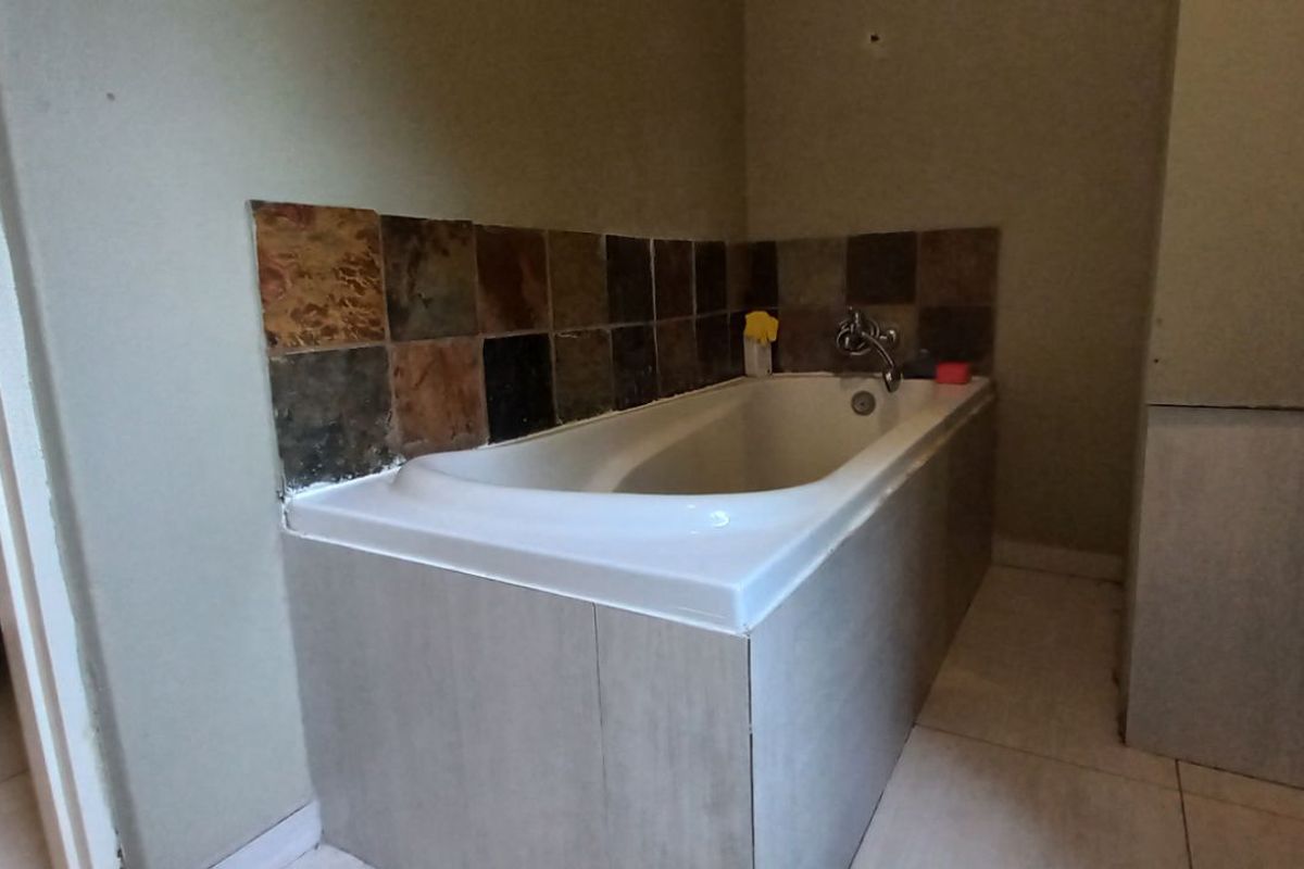 A bathroom featuring a built-in bathtub with decorative stone-look tile splashback and a pedestal basin.