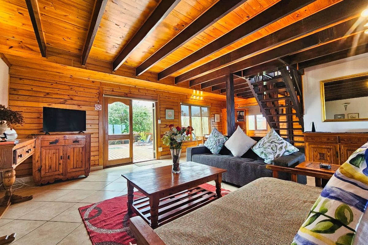 Spacious living room featuring exposed timber ceiling beams, tiled flooring, and a wooden staircase leading to the upper level with direct patio access.