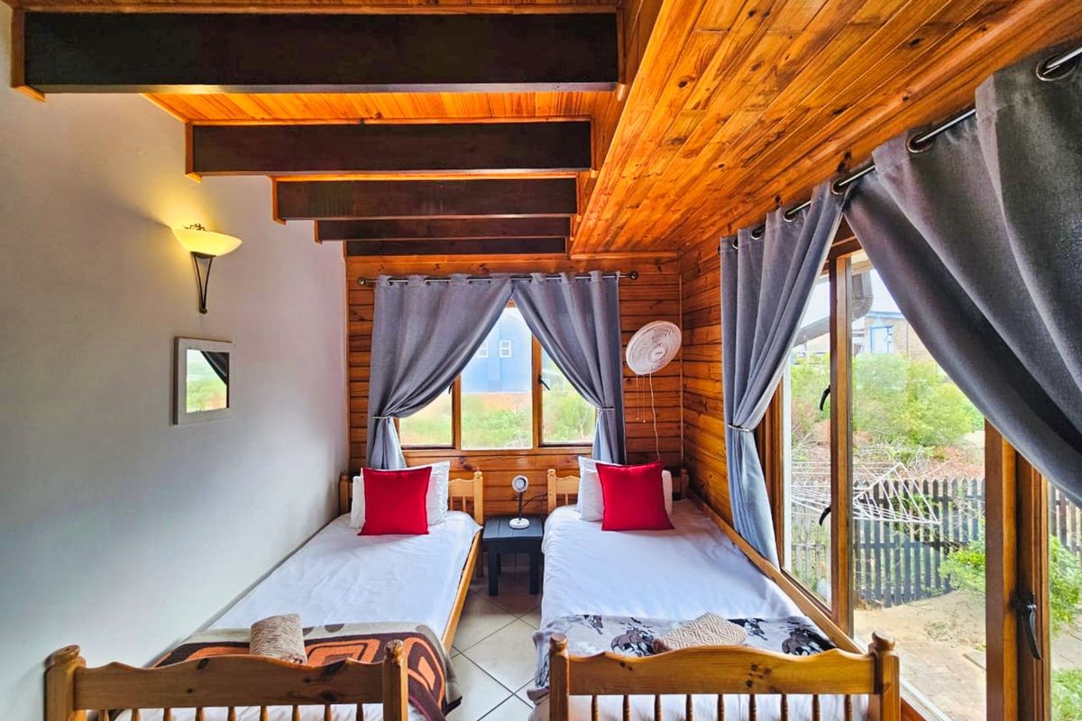 A cozy bedroom featuring exposed timber ceiling beams, wood-paneled walls, and large windows that provide natural light and garden views.