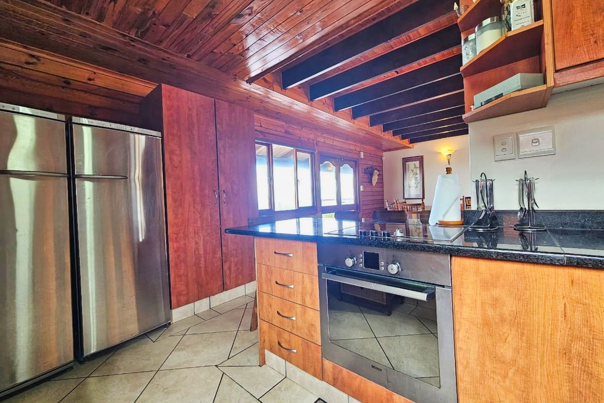 A kitchen featuring wooden cabinetry, granite countertops, a built-in oven, and a distinctive timber-clad ceiling with exposed beams.