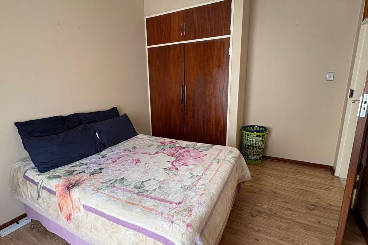 A bedroom featuring built-in wooden cupboards and laminate flooring, providing a functional and neutral space for rest.