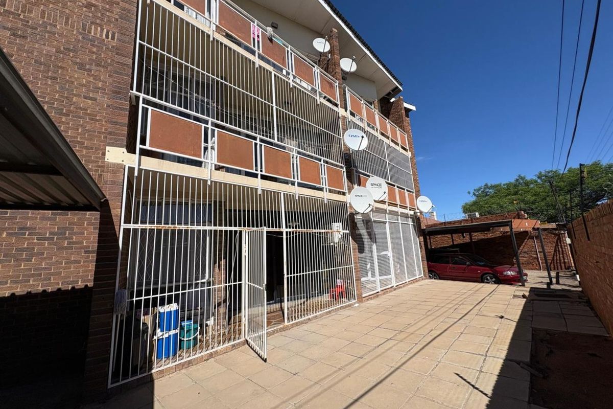 Exterior view of the apartment building featuring a paved ground floor patio area and security gates on the lower and upper levels.