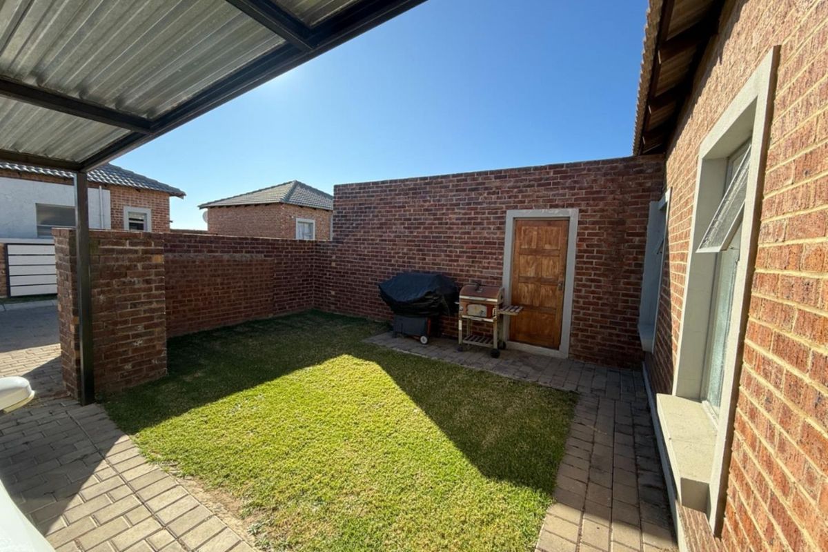 A private rear courtyard featuring a paved patio area, a small lawn, and a covered section, enclosed by face-brick boundary walls.