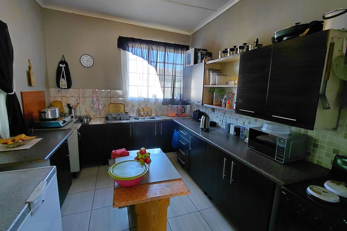 A functional kitchen featuring dark cabinetry, tiled splashbacks, a double sink, and tiled flooring, providing a practical workspace for daily meal preparation.