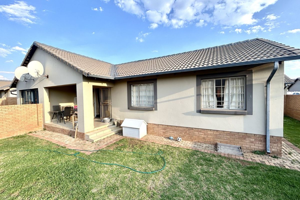 Rear view of the townhouse featuring a covered patio, tiled roof, brick base, and a private garden area.