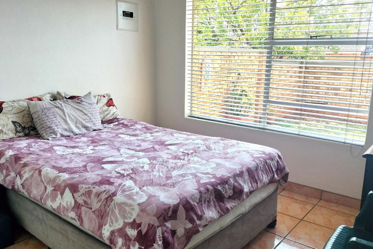 A bedroom featuring tiled flooring, a large window with fitted blinds, and a wall-mounted electrical distribution board.