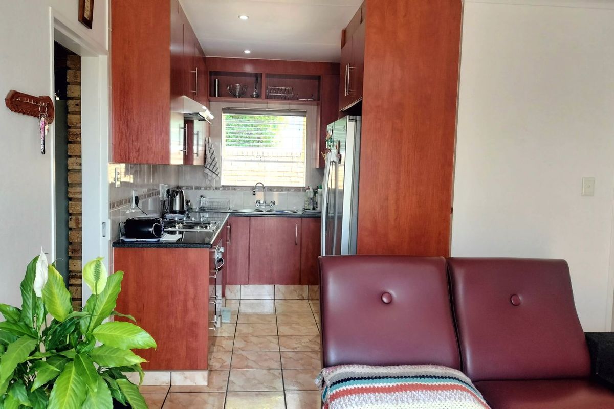 A compact kitchen featuring cherry wood cabinetry, dark granite countertops, and tiled flooring, conveniently positioned adjacent to the living area.