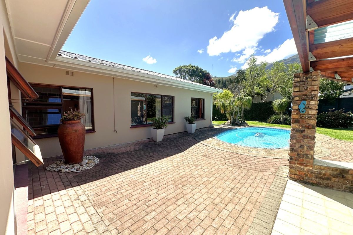 A spacious rear patio area featuring brick paving, a swimming pool, and a covered pergola structure, offering a pleasant outdoor living space.
