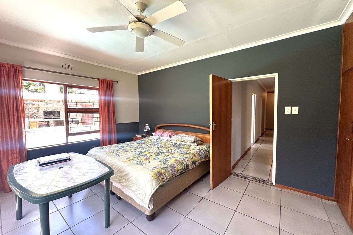 A spacious bedroom featuring tiled flooring, a ceiling fan, and built-in cupboards, with direct access to the hallway.