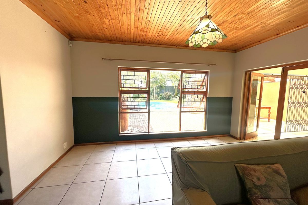 Living room featuring tiled flooring, a timber-clad ceiling, and large windows providing a view of the outdoor pool area.