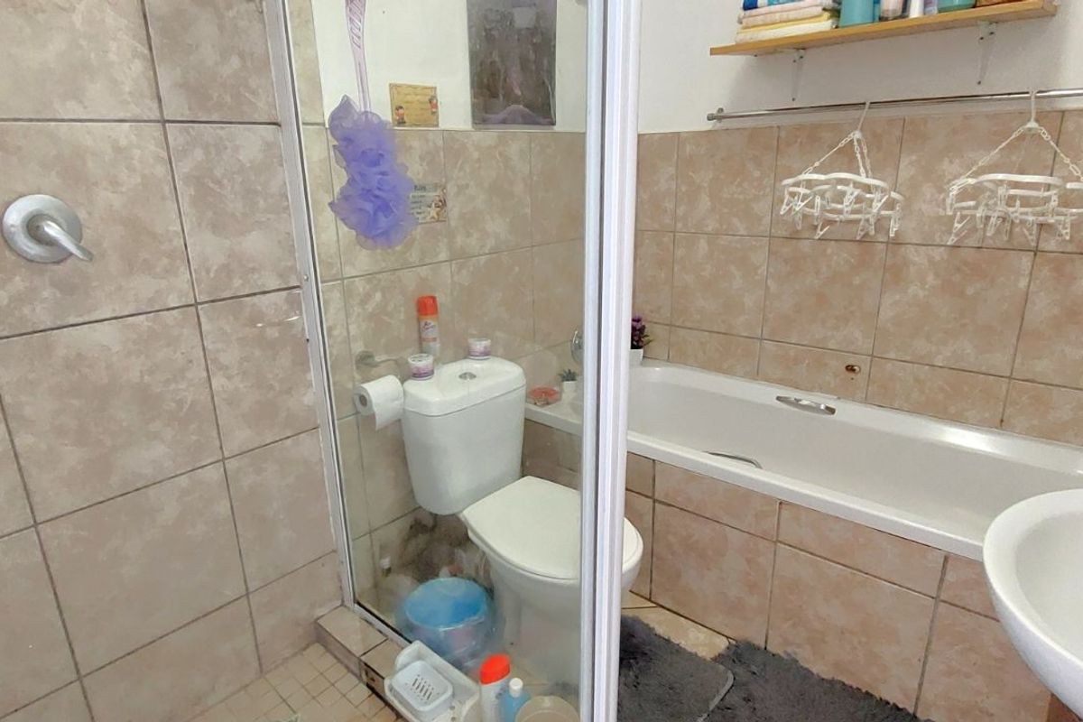 A functional bathroom featuring a combined shower and bathtub unit, a standard toilet, and a wall-mounted basin with tiled walls.