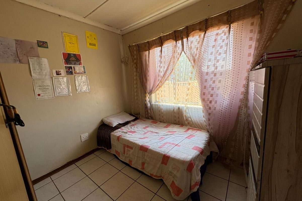 A compact bedroom featuring tiled flooring, a window with curtain fixtures, and standard electrical outlets.