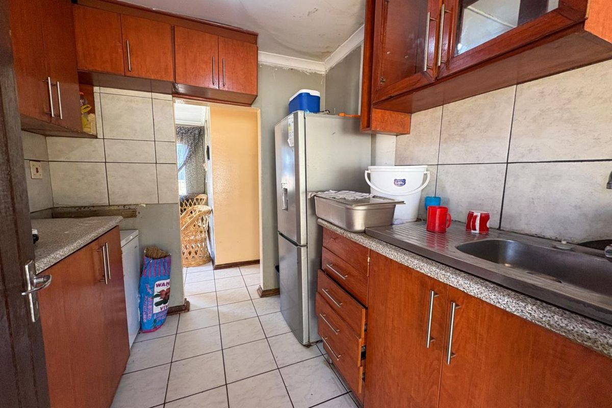 A compact kitchen featuring wooden cabinetry, tiled flooring, and a stainless steel sink, offering a functional layout with potential for modernization.