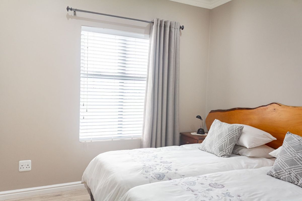 A well-maintained bedroom featuring neutral wall tones, laminate flooring, and a window fitted with blinds and curtain rod.