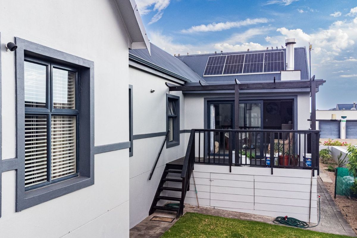 Rear view of the property featuring a raised timber deck, staircase, solar panels, and modern exterior finishes.