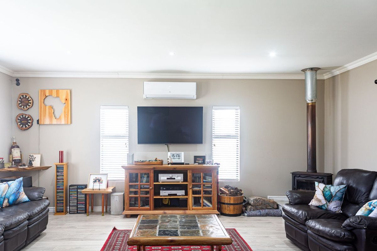 A comfortable living room featuring a built-in wood-burning fireplace, wall-mounted air conditioning unit, and dual windows providing natural light.