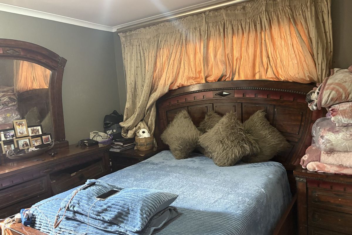 A bedroom featuring a large wooden headboard and matching dresser, with full-length curtains covering the window area.