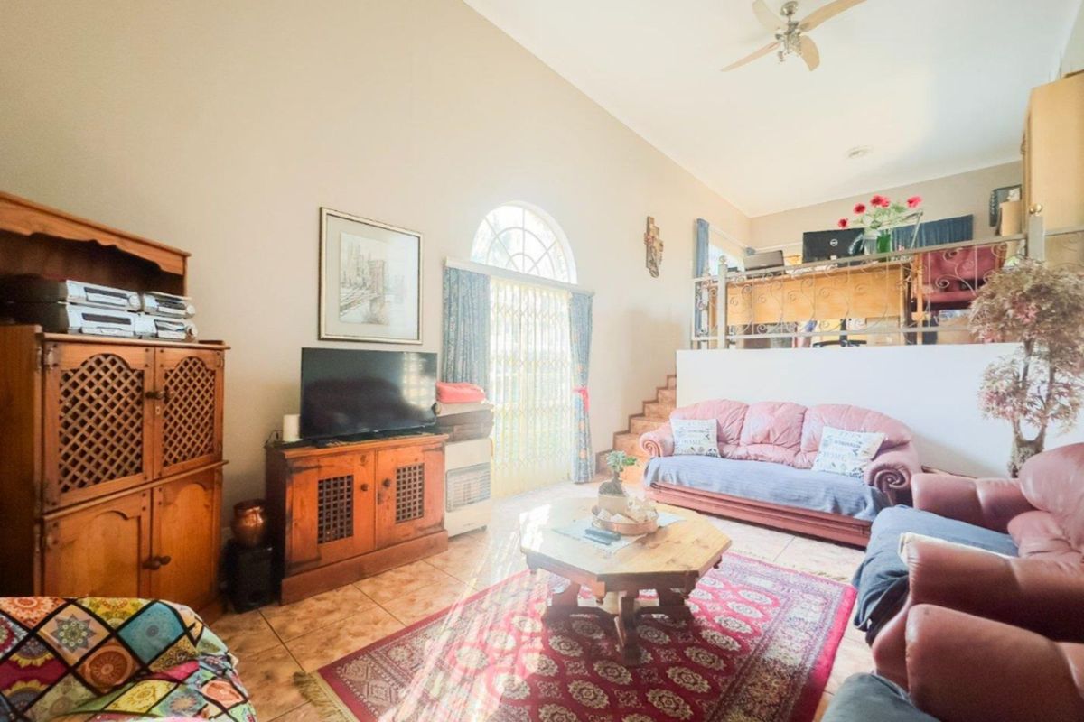 Spacious living room featuring high vaulted ceilings, tiled flooring, and an arched window with security gate, leading to an elevated mezzanine level.