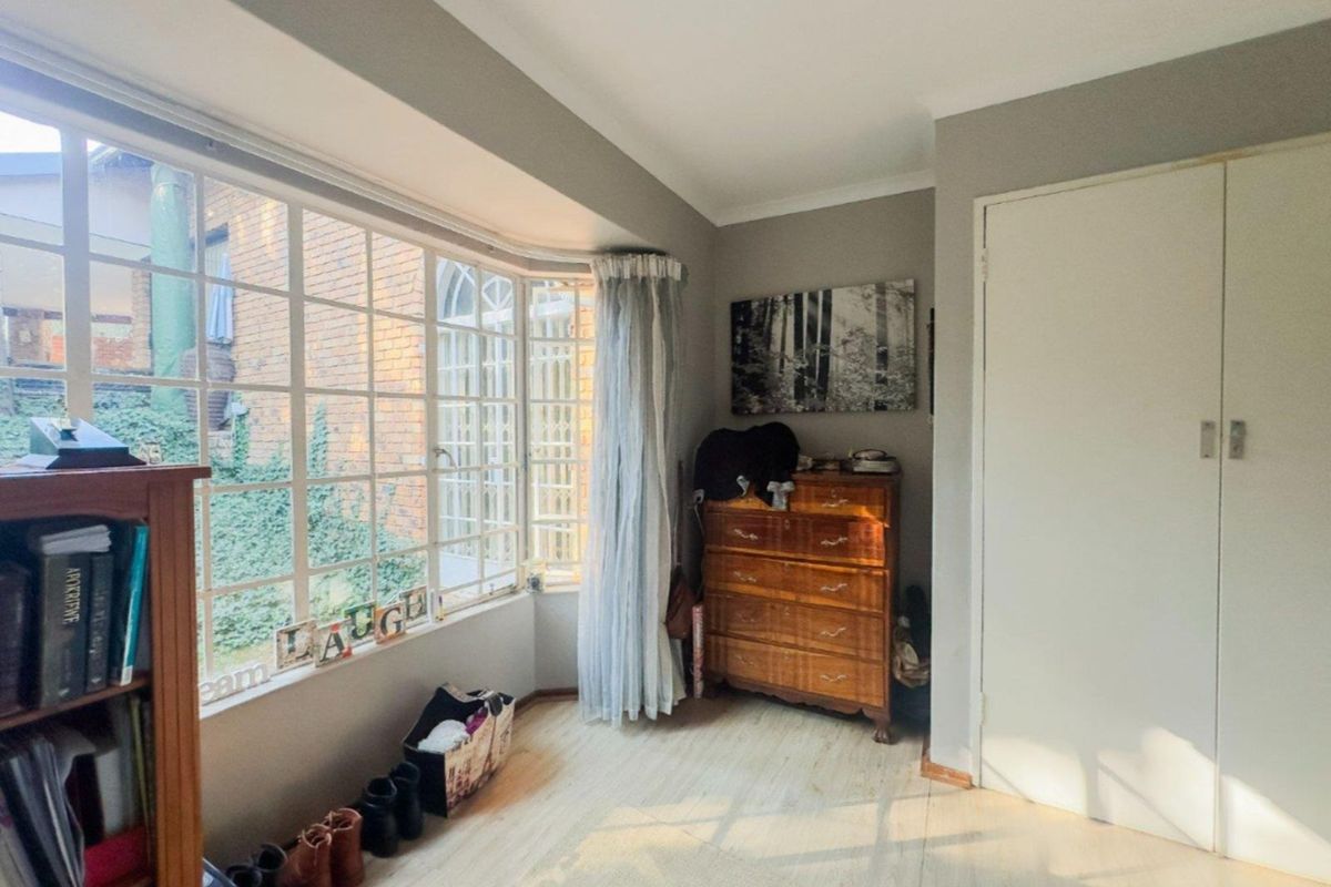 A bedroom featuring a large bay window, built-in cupboard, and light-toned flooring, offering natural light and a view of the exterior brick wall.