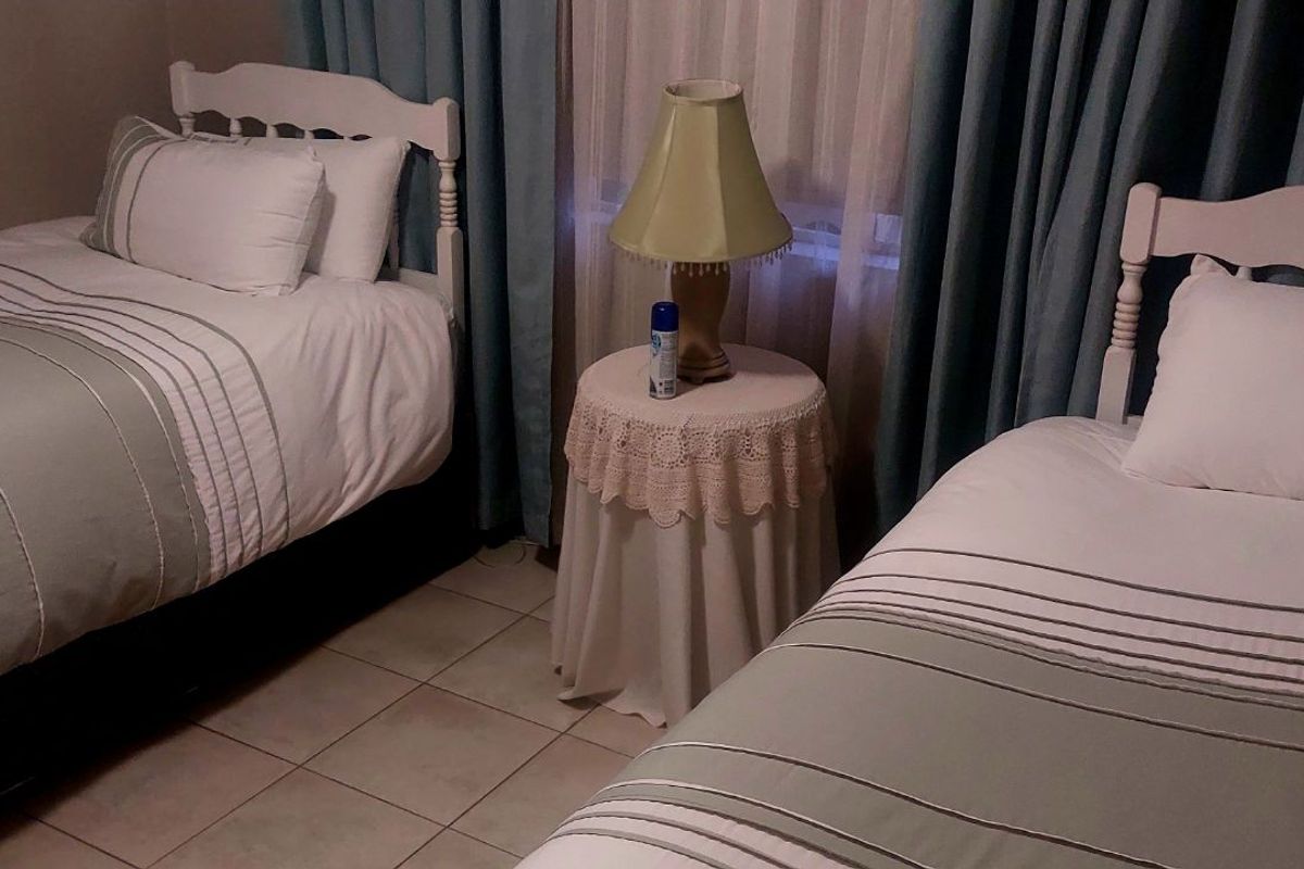 A bedroom featuring tiled flooring and window treatments, currently configured with two single beds.