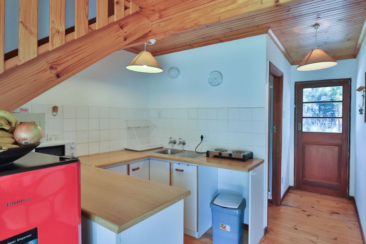 Compact kitchen area featuring timber ceiling, wooden staircase, tiled splashback, and direct access to an exterior door.