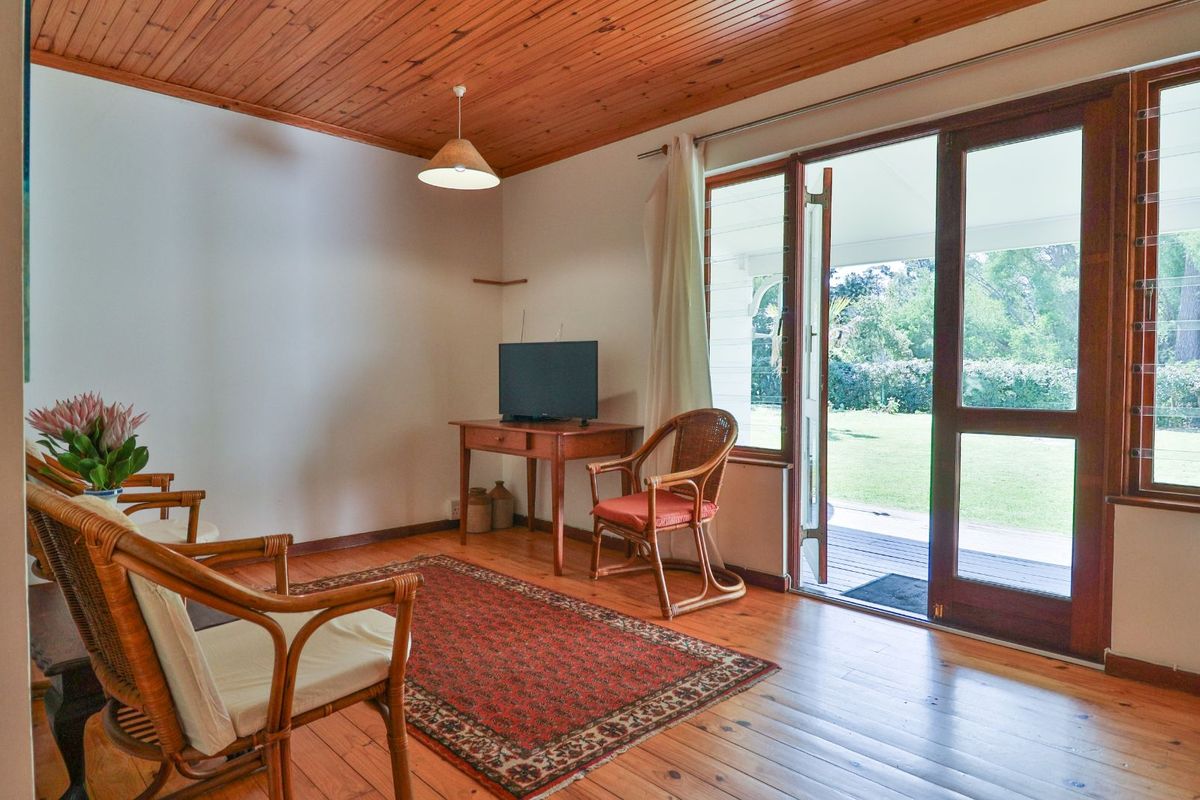 A living room featuring timber flooring and a wood-paneled ceiling, with large glass doors providing direct access to the outdoor patio and garden.