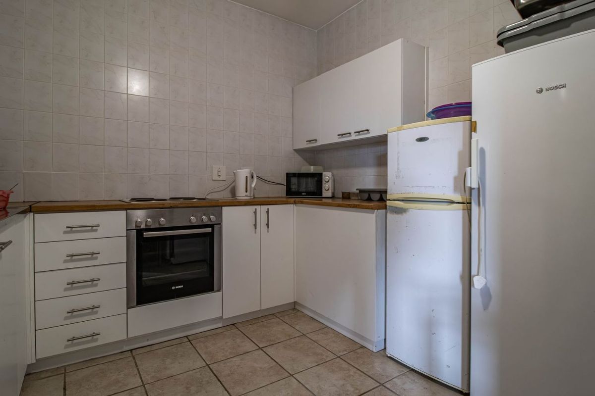 A functional kitchen featuring white cabinetry, a built-in oven, a hob, and tiled flooring, offering a practical layout for daily meal preparation.