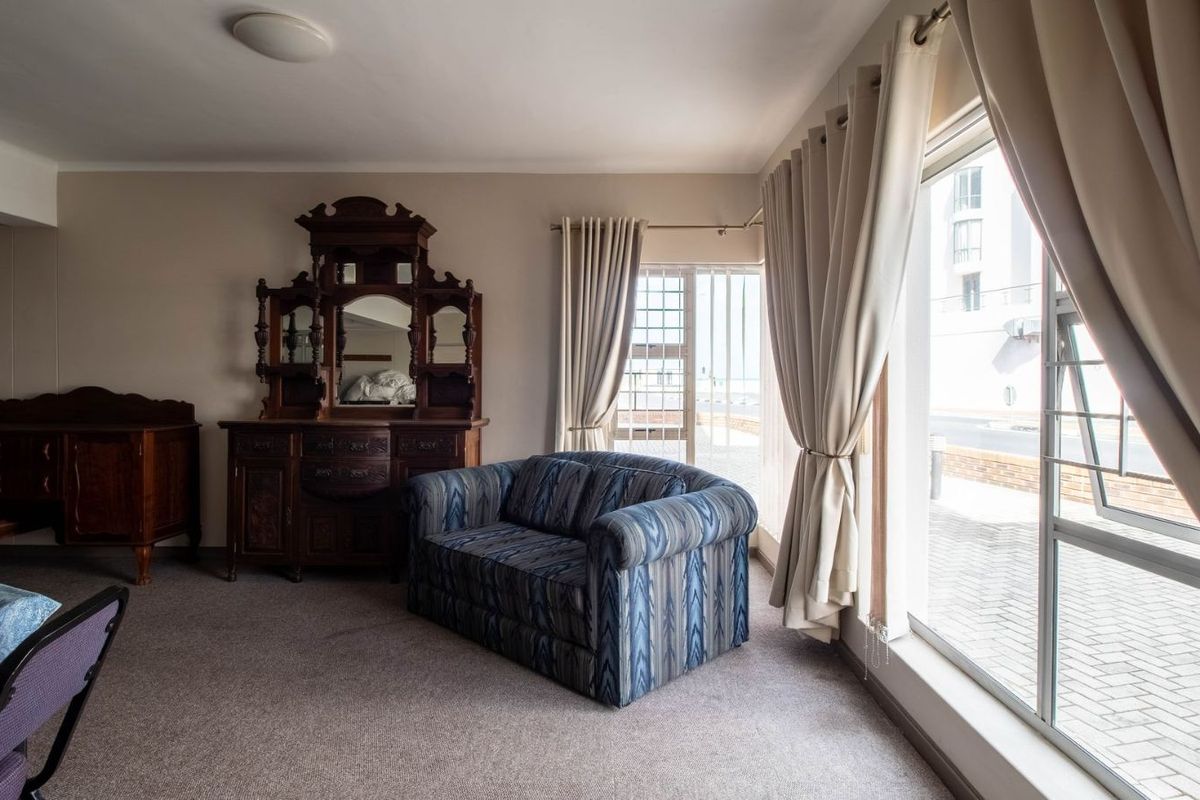 A living room area featuring large windows with curtains, carpeted flooring, and access to an outdoor space.