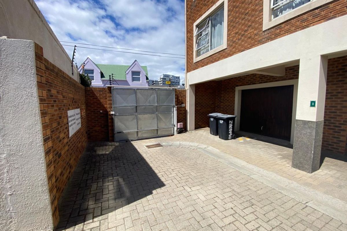 A private paved courtyard area featuring a secure metal gate, brick boundary walls, and direct access to a covered garage entrance.