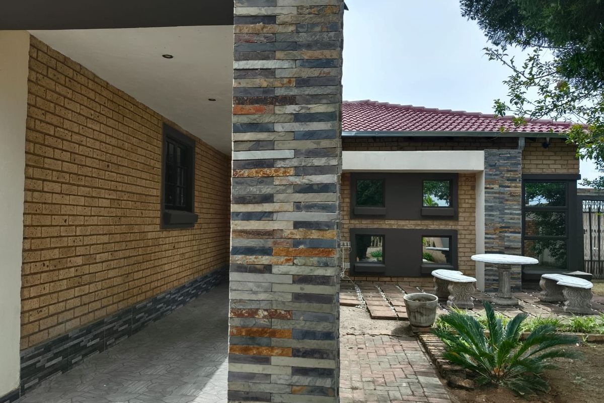 A well-maintained exterior rear view featuring a covered patio, decorative stone cladding, face brick walls, and a paved courtyard area.