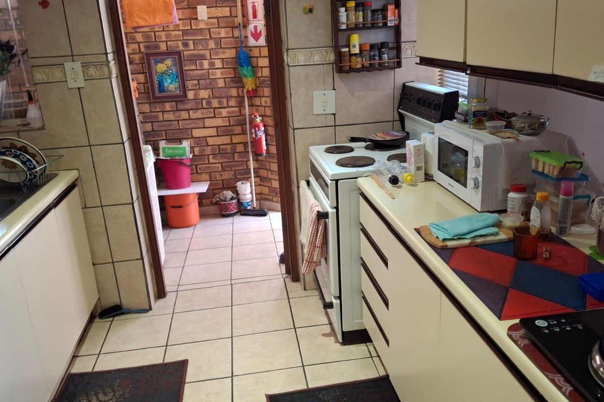 A functional kitchen featuring tiled flooring, built-in cabinetry, and a freestanding stove, with an adjacent utility area showcasing exposed brickwork.