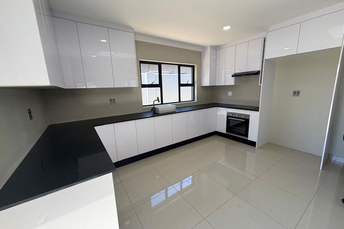 Modern kitchen featuring high-gloss white cabinetry, contrasting black stone countertops, integrated oven, extractor fan, and sleek tiled flooring.