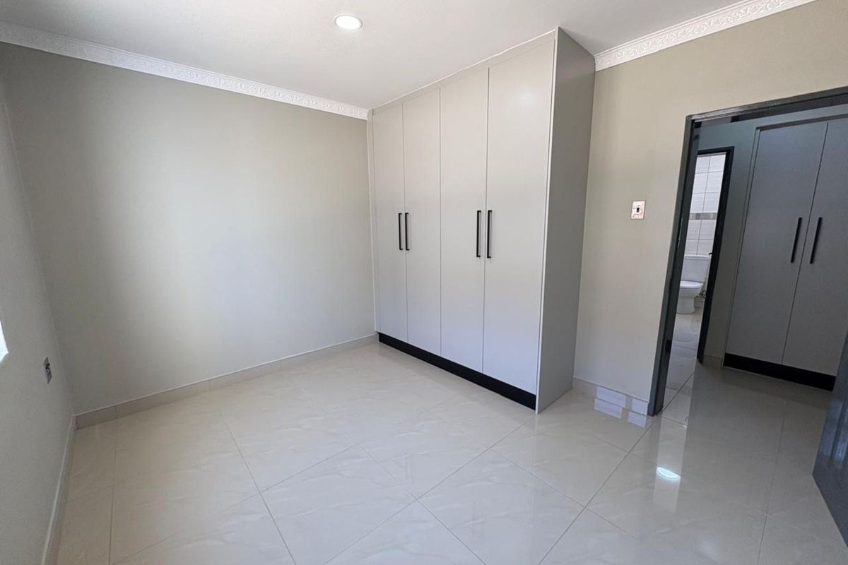 A bright, modern bedroom featuring neutral walls, polished tile flooring, and built-in floor-to-ceiling cabinetry with sleek black handles.