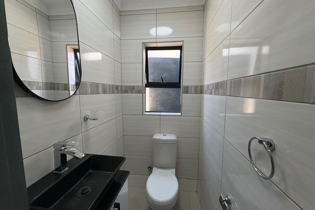 A modern, compact bathroom featuring floor-to-ceiling tiled walls, a contemporary black vessel sink with chrome faucet, and a white toilet.