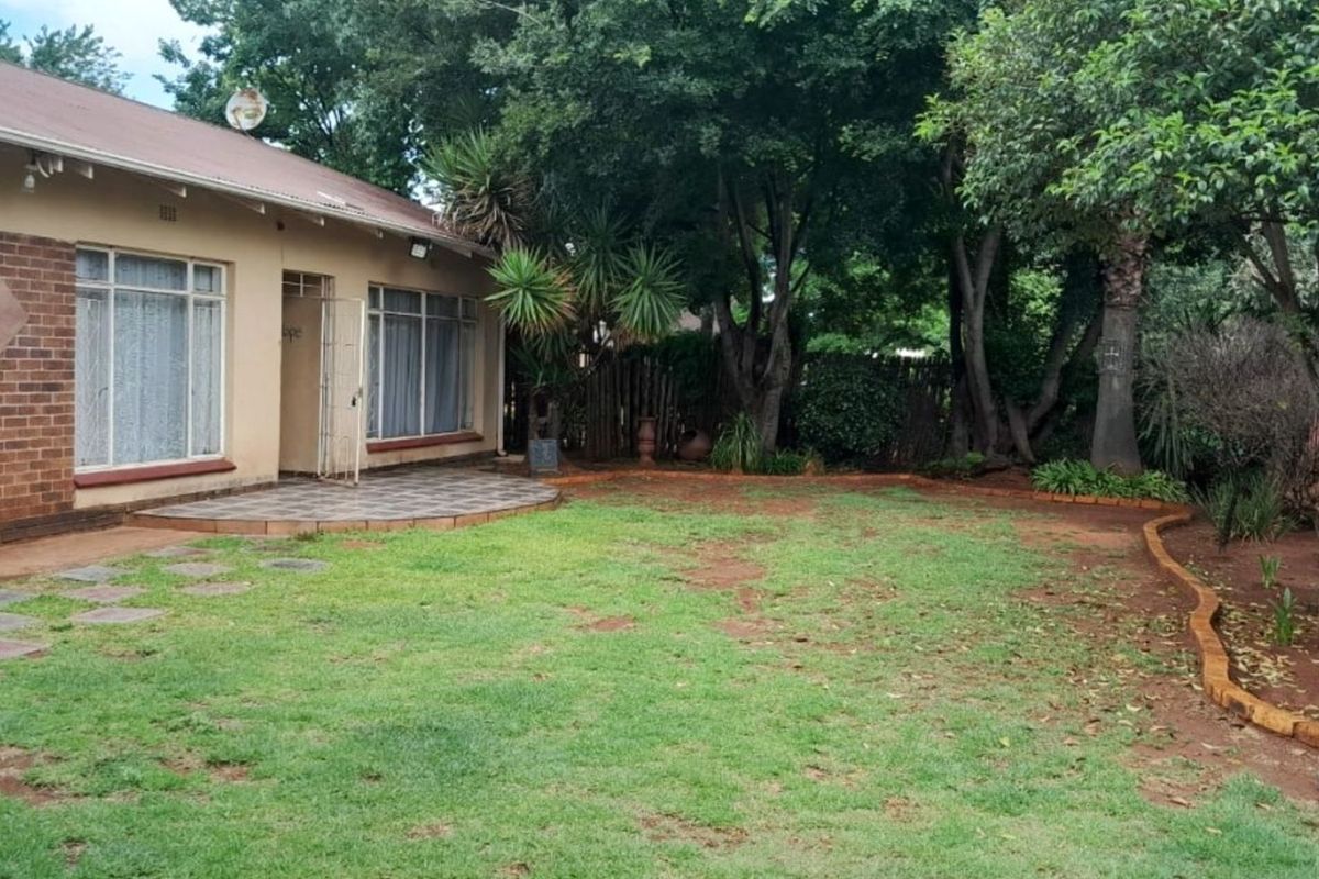 A spacious rear garden featuring a paved patio area, established trees, and a lawn, providing a private outdoor space for the home.