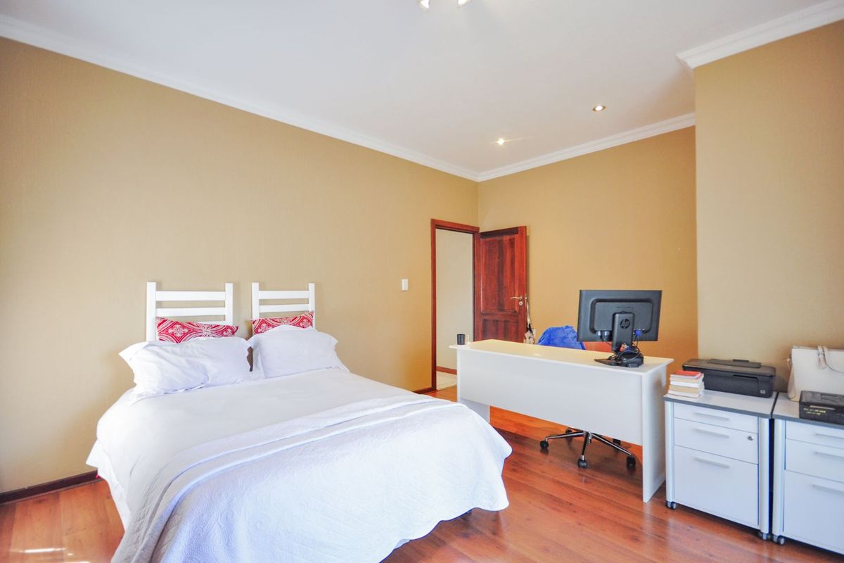 A bedroom featuring warm-toned walls, timber flooring, and recessed ceiling lighting, providing a functional space for rest and work.