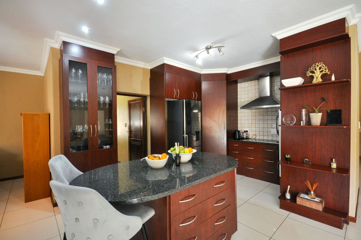 A well-appointed kitchen featuring dark wood cabinetry, granite countertops, a central island with breakfast seating, and a stainless steel extractor fan.