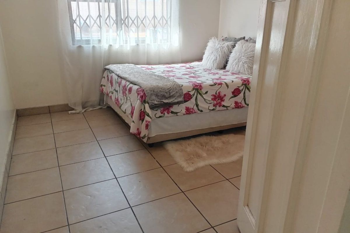 A bedroom featuring tiled flooring and a window fitted with security bars.
