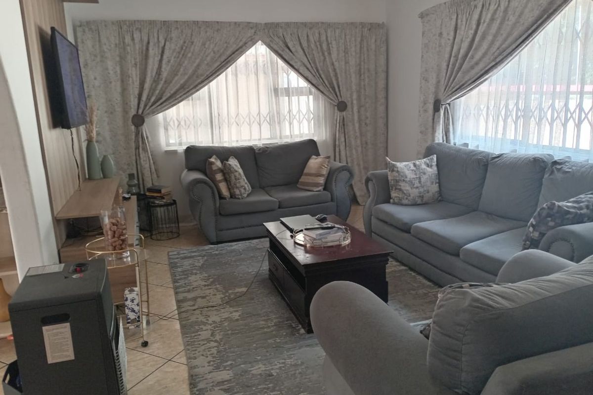 A comfortable living room featuring tiled flooring, built-in cabinetry for media storage, and large windows with security gates.