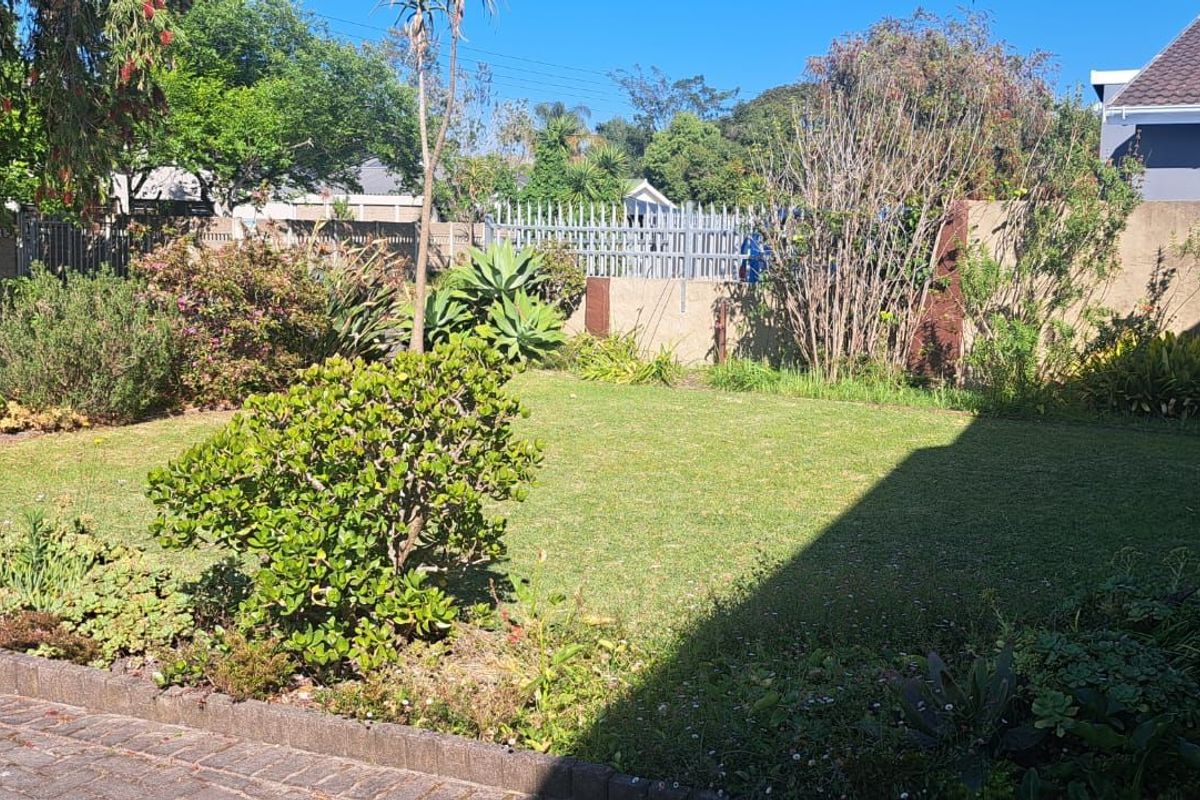 A private rear garden featuring a lawn area, established landscaping, and secure boundary walling with metal fencing.