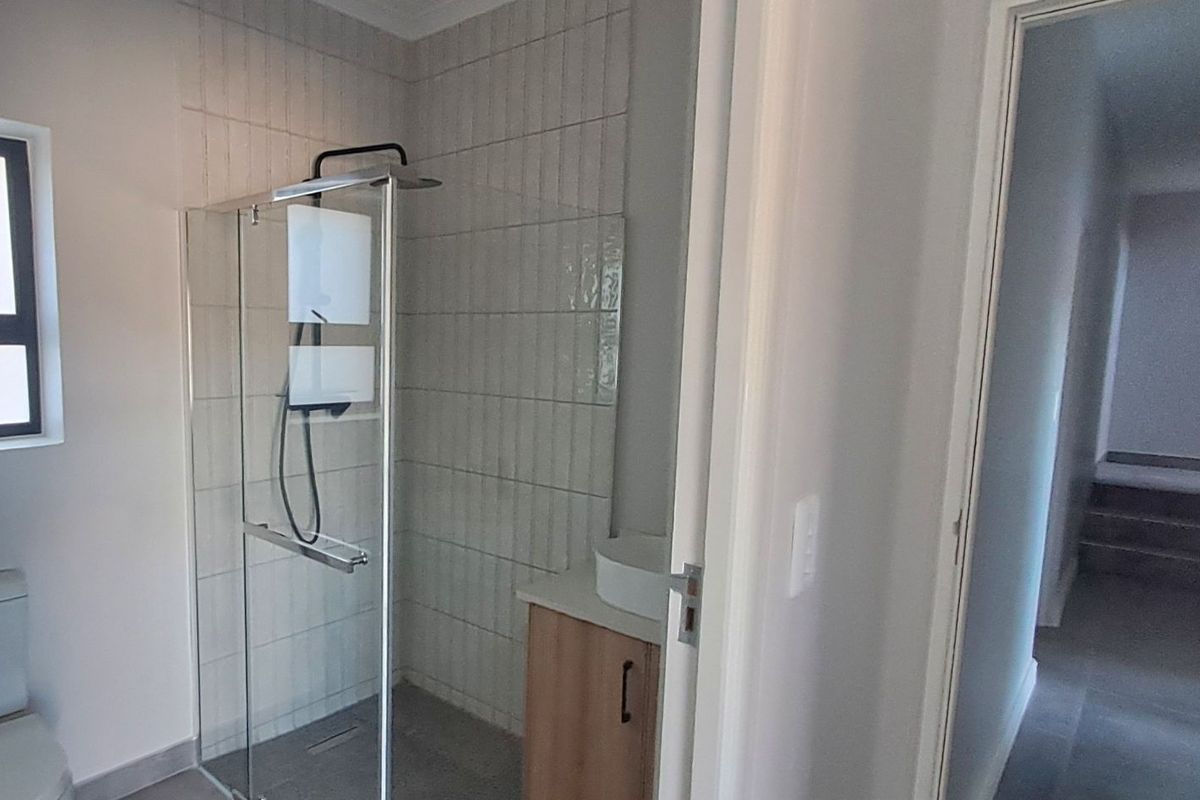A modern bathroom featuring a glass-enclosed shower with vertical wall tiling, a vanity unit with a vessel sink, and a toilet.
