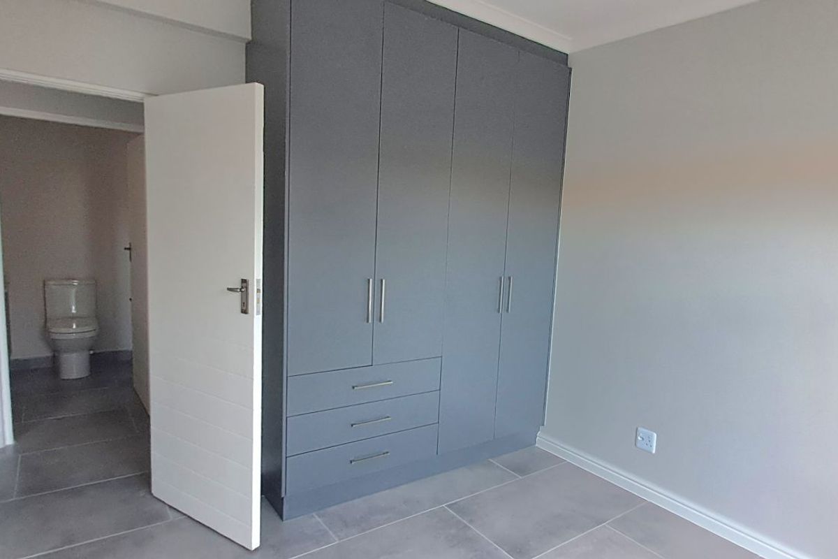 A modern bedroom featuring built-in grey cabinetry and tiled flooring, with an adjacent en-suite bathroom visible through the doorway.