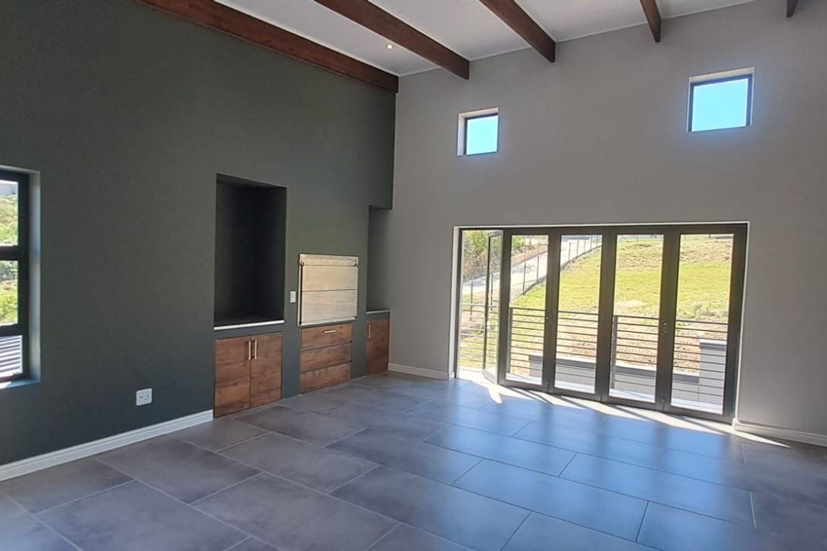 Spacious living area featuring high vaulted ceilings with exposed timber beams, large glass stacker doors, and a built-in indoor braai unit.