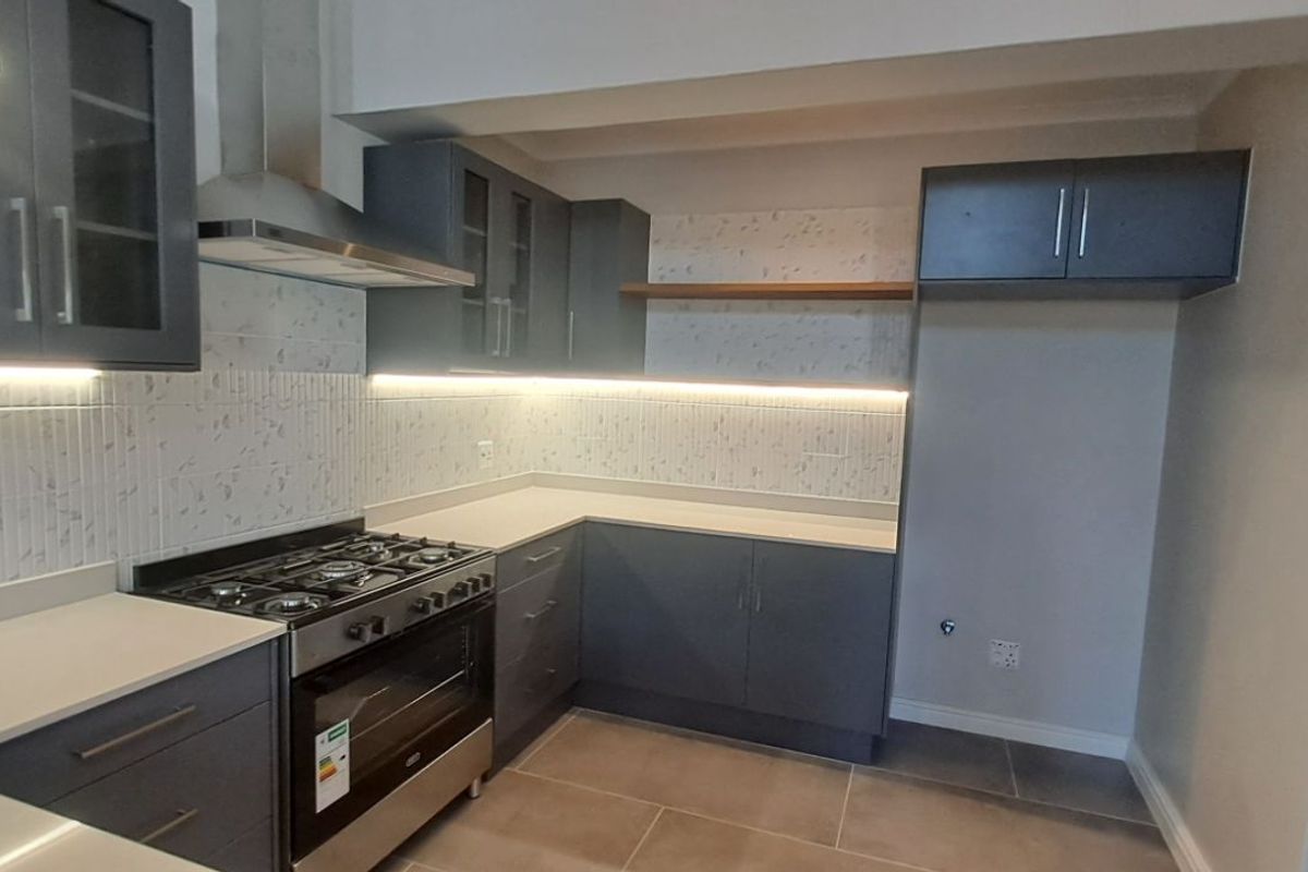 Modern kitchen featuring dark grey cabinetry, stone countertops, integrated under-cabinet lighting, and a stainless steel gas stove with extractor fan.