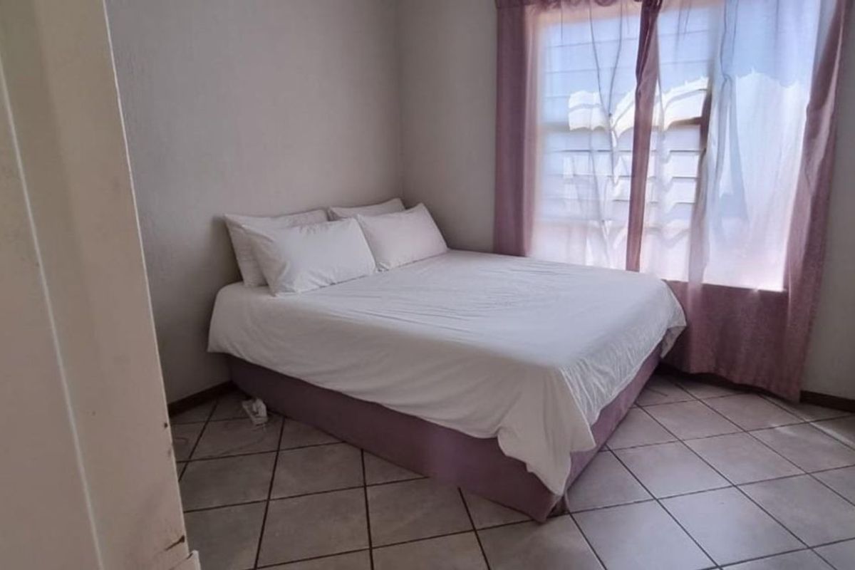 A compact bedroom featuring tiled flooring and a window with fitted security bars, offering a functional and simple living space.