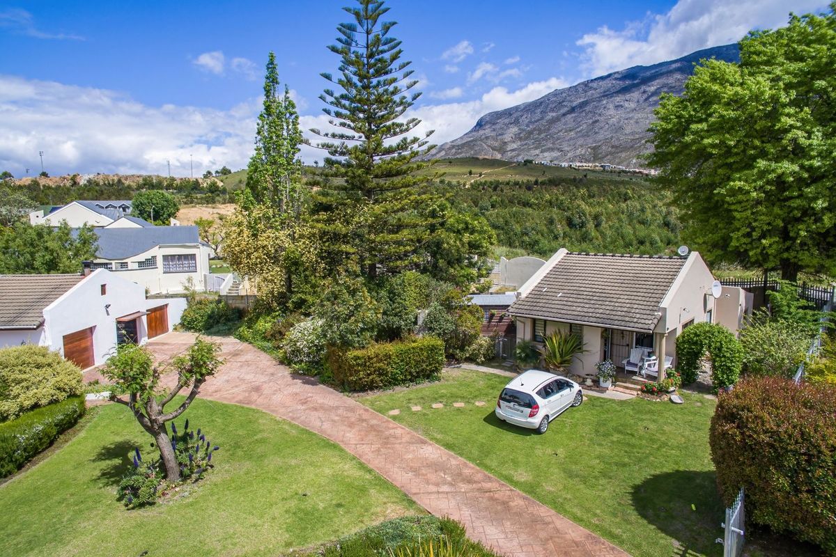 Aerial view of a residential property featuring a paved driveway, landscaped garden, and mountain backdrop.