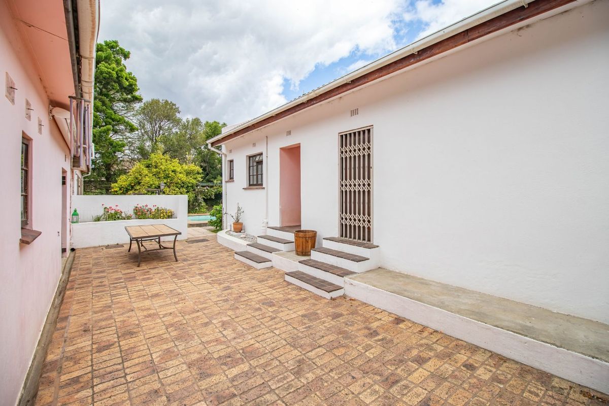A paved rear courtyard area featuring a raised planter bed, concrete steps leading to the dwelling, and access to the garden and pool area.