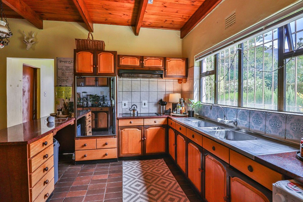 A traditional kitchen featuring wooden cabinetry, exposed timber ceiling beams, tiled flooring, and a double stainless steel sink with a large window view.