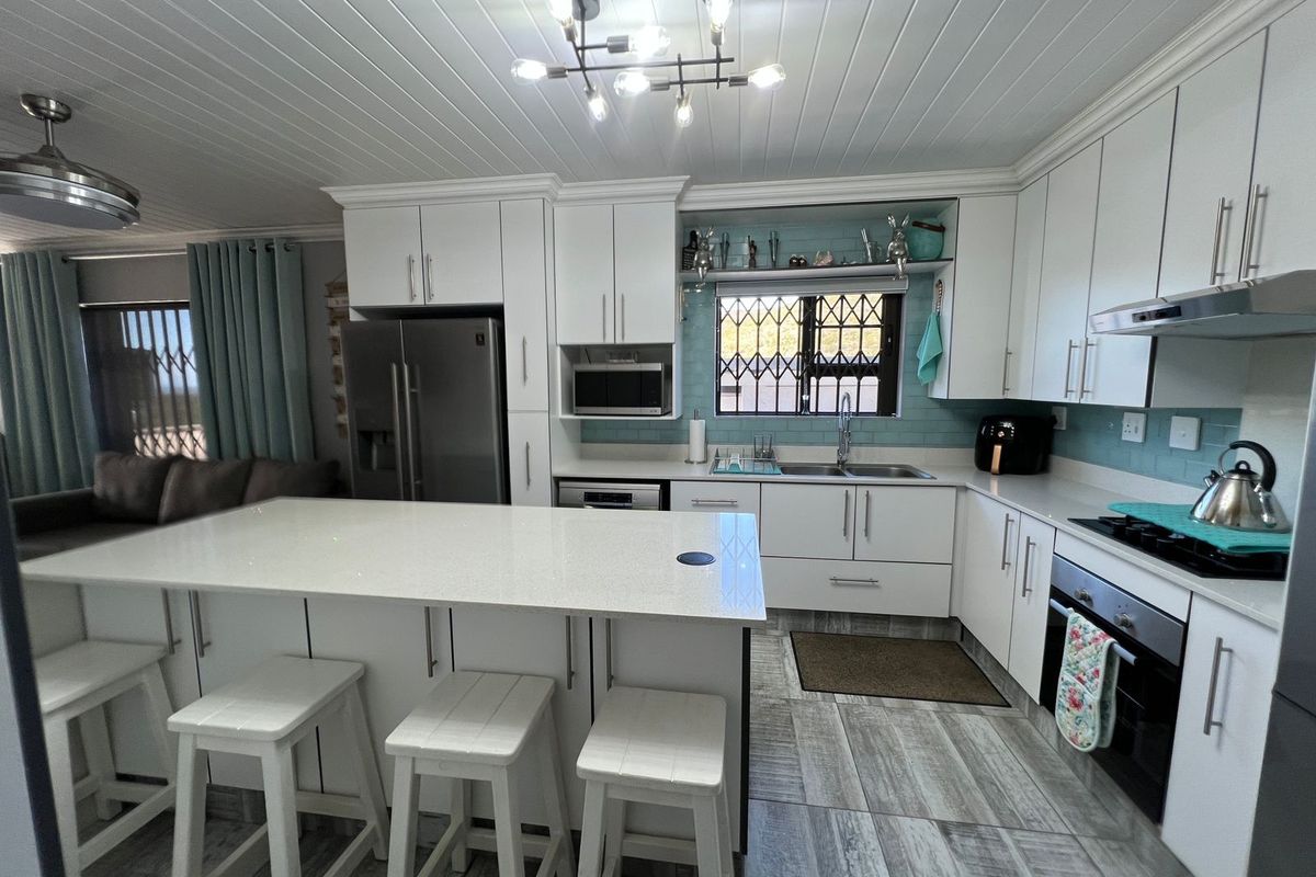 Modern kitchen featuring white cabinetry, stone countertops, a central island, integrated oven, and a tiled backsplash with a window overlooking the exterior.